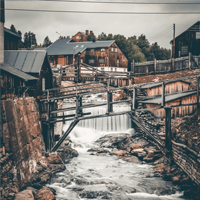 Old mill with water flowing through, surrounded by trees and buildings.