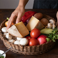 Hand reaching into a basket of fruits and vegetables on a wooden table