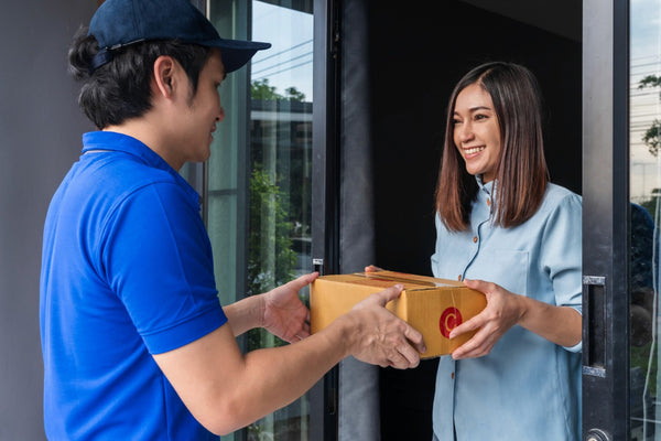 Delivery person in blue uniform handing over a package to a woman at a door.