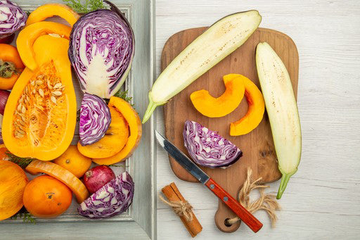 Assorted vegetables including squash, eggplant, and cabbage on a wooden cutting board with a knife.
