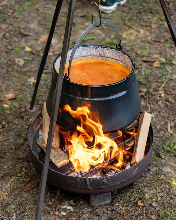 Black pot over an open fire with flames and wooden kindling.