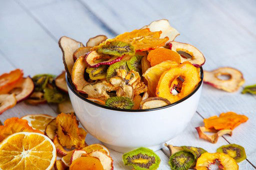 Assorted dried fruits in a white bowl on a light wooden surface